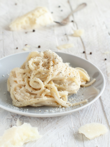 a white plate of gluten free cacio e pepe on a white table