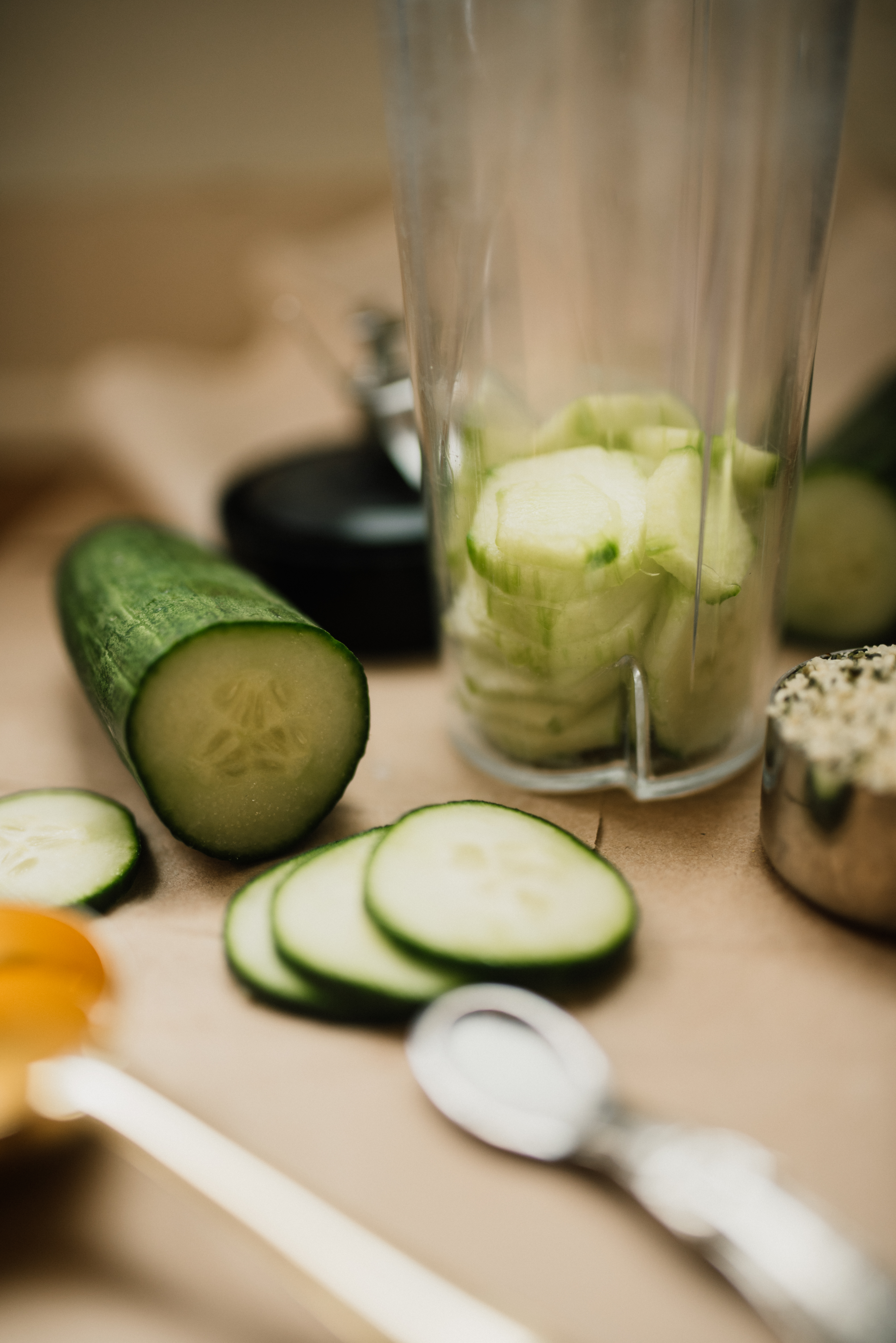 a blender cup of sliced cucumbers next to a teaspoon of salt and some hemp hearts