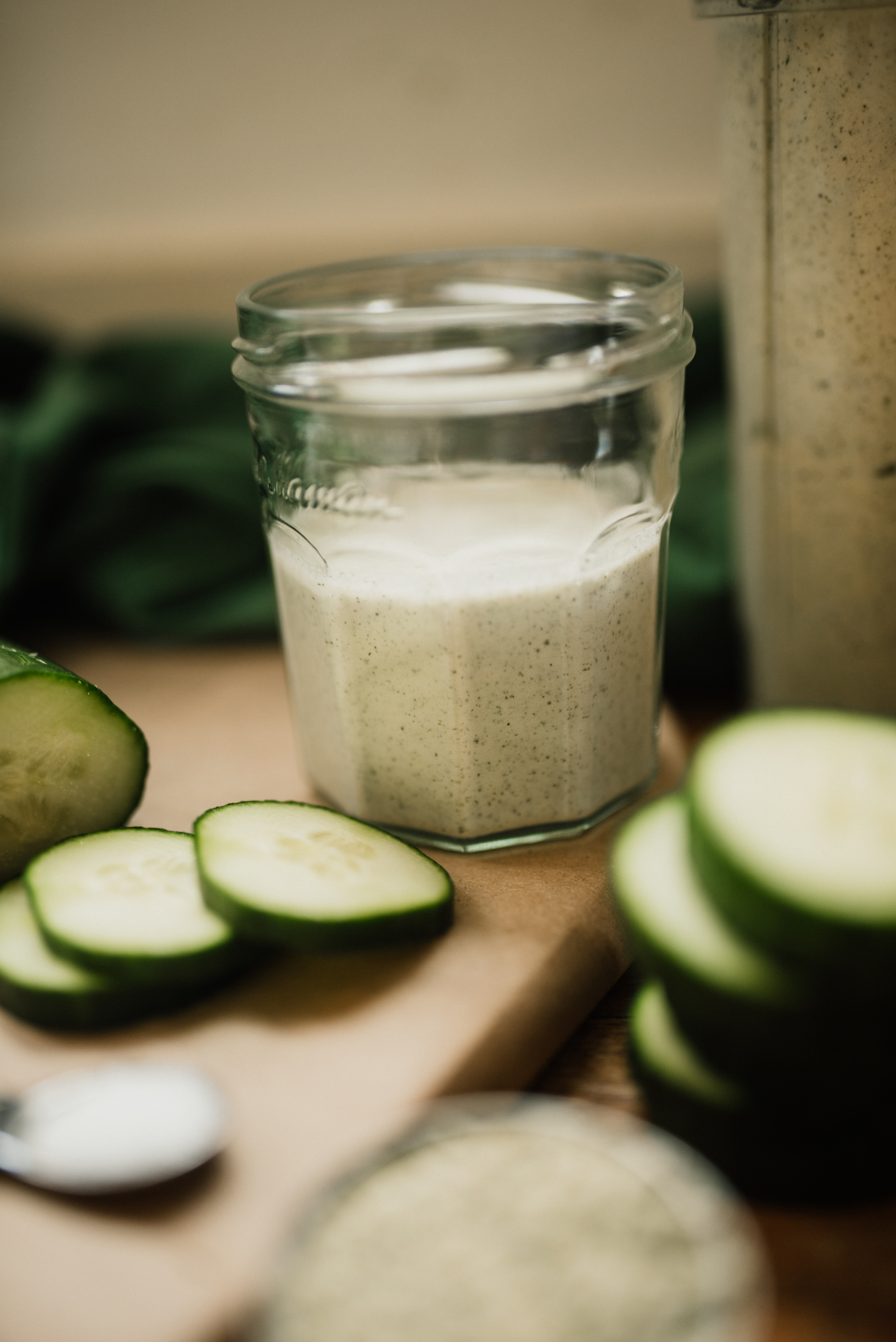 a cup of prepared alkaline salad dressing with the blender cup behind and chopped cucumbers in front