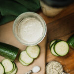 a jar of alkaline cucumber hemp dressing next to all the ingredients: sliced cucumbers, salt, ACV, and hemp hearts