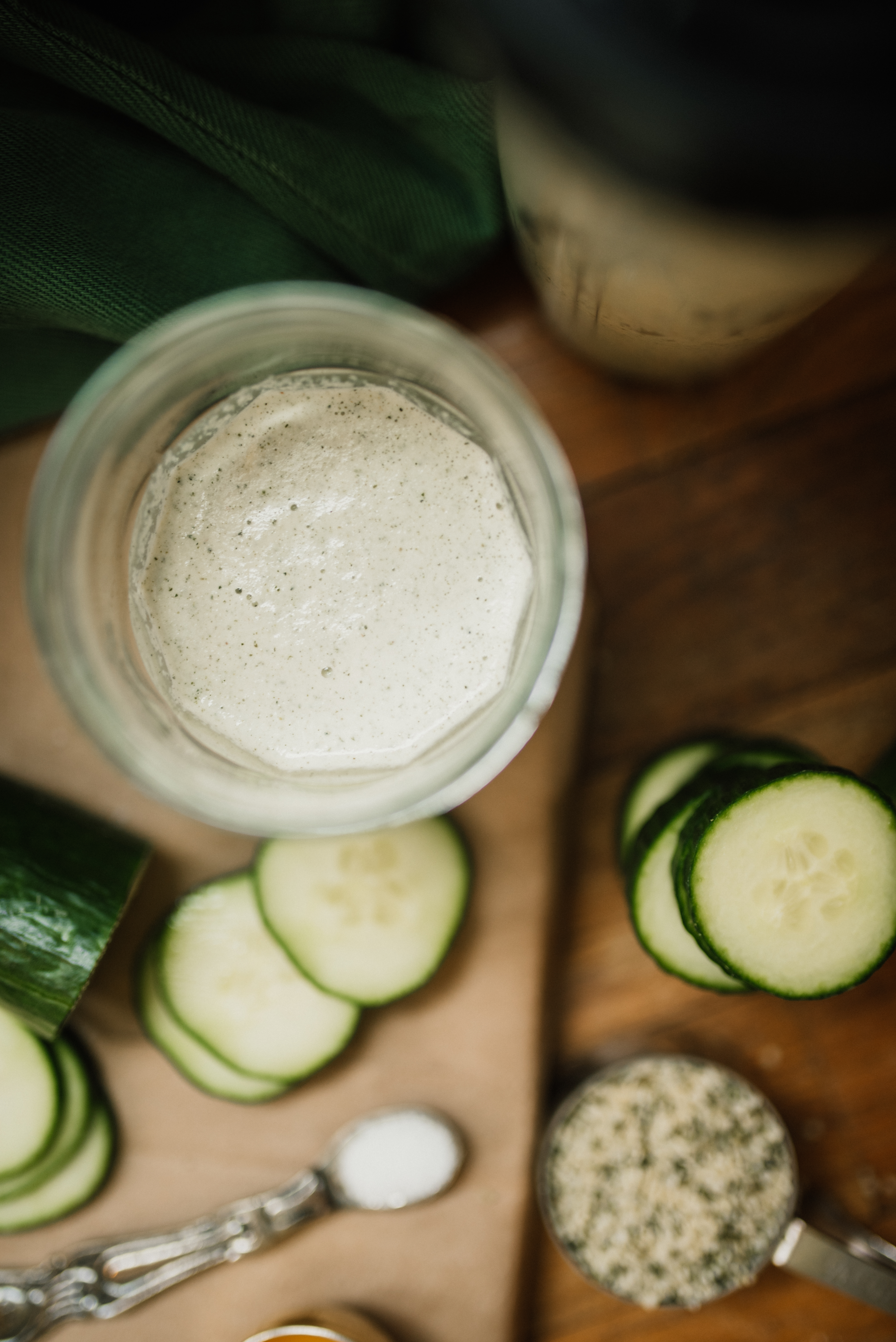 a cup of prepared alkaline salad dressing with the blender cup behind and chopped cucumbers in front