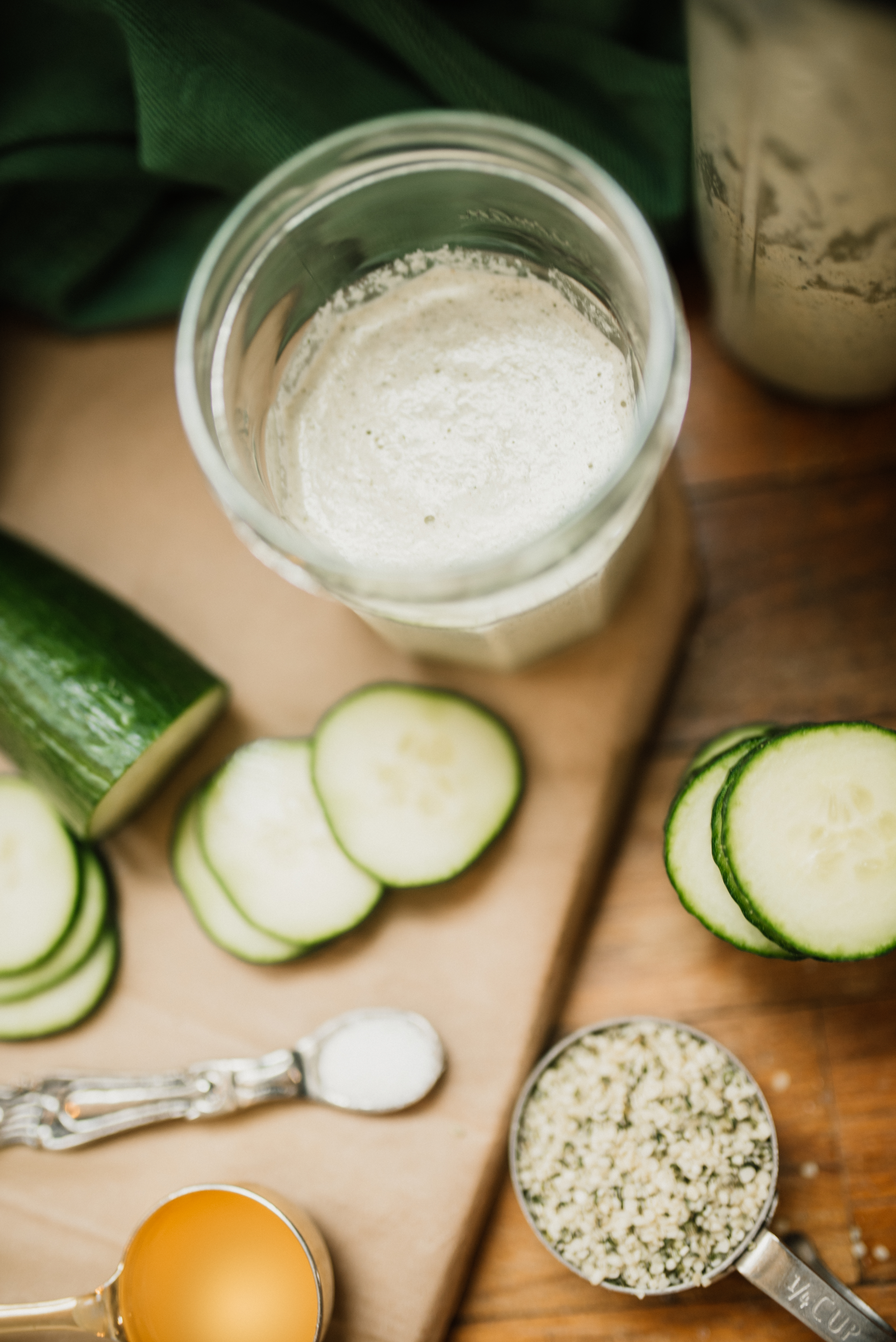 a jar of alkaline cucumber hemp dressing next to all the ingredients: sliced cucumbers, salt, ACV, and hemp hearts