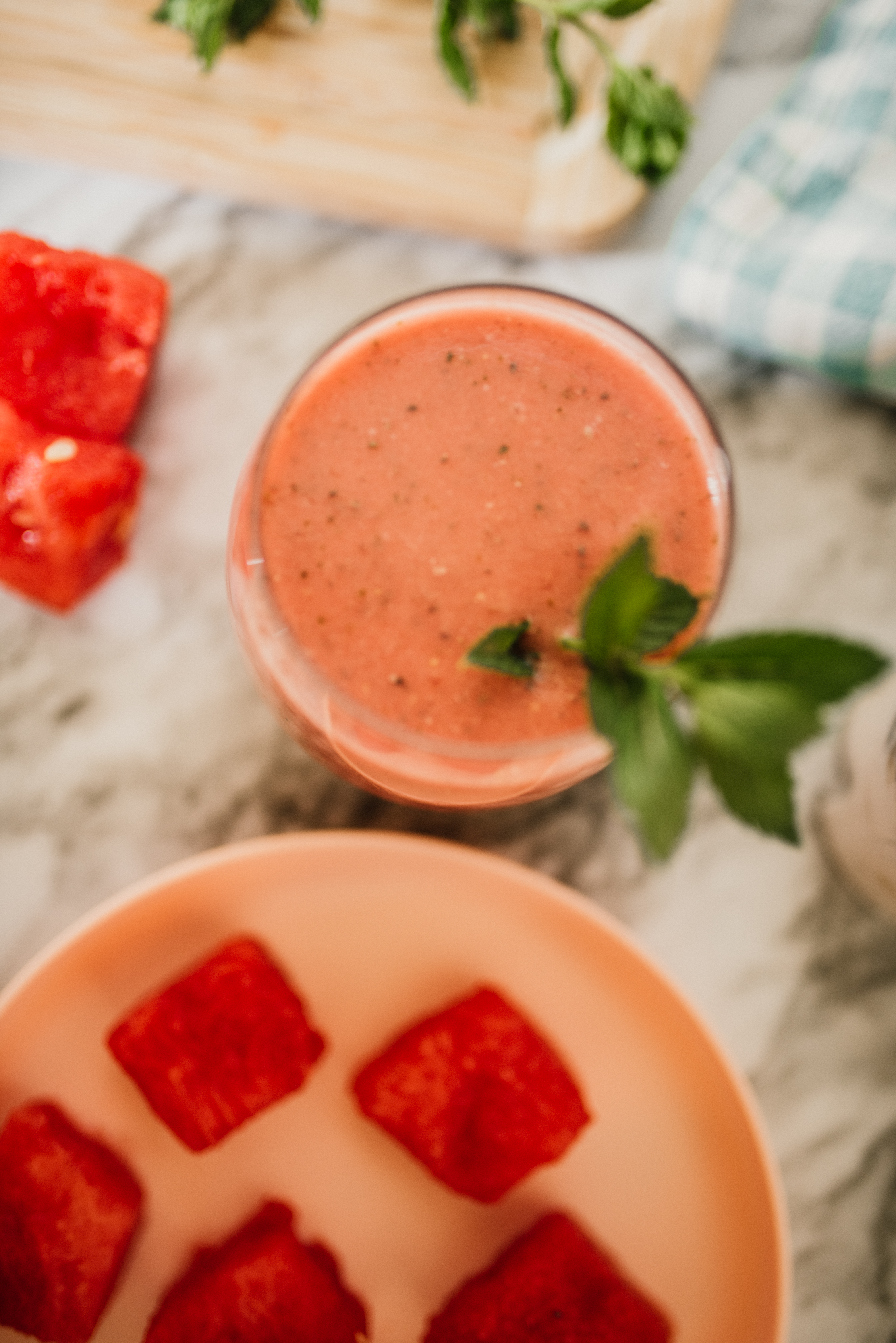 a cup of watermelon smoothie surrounded by a plate of chopped watermelon