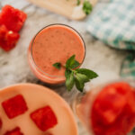 a watermelon smoothie for weight loss on a table with a smoothie cup of ingredients and a plate of chopped watermelon