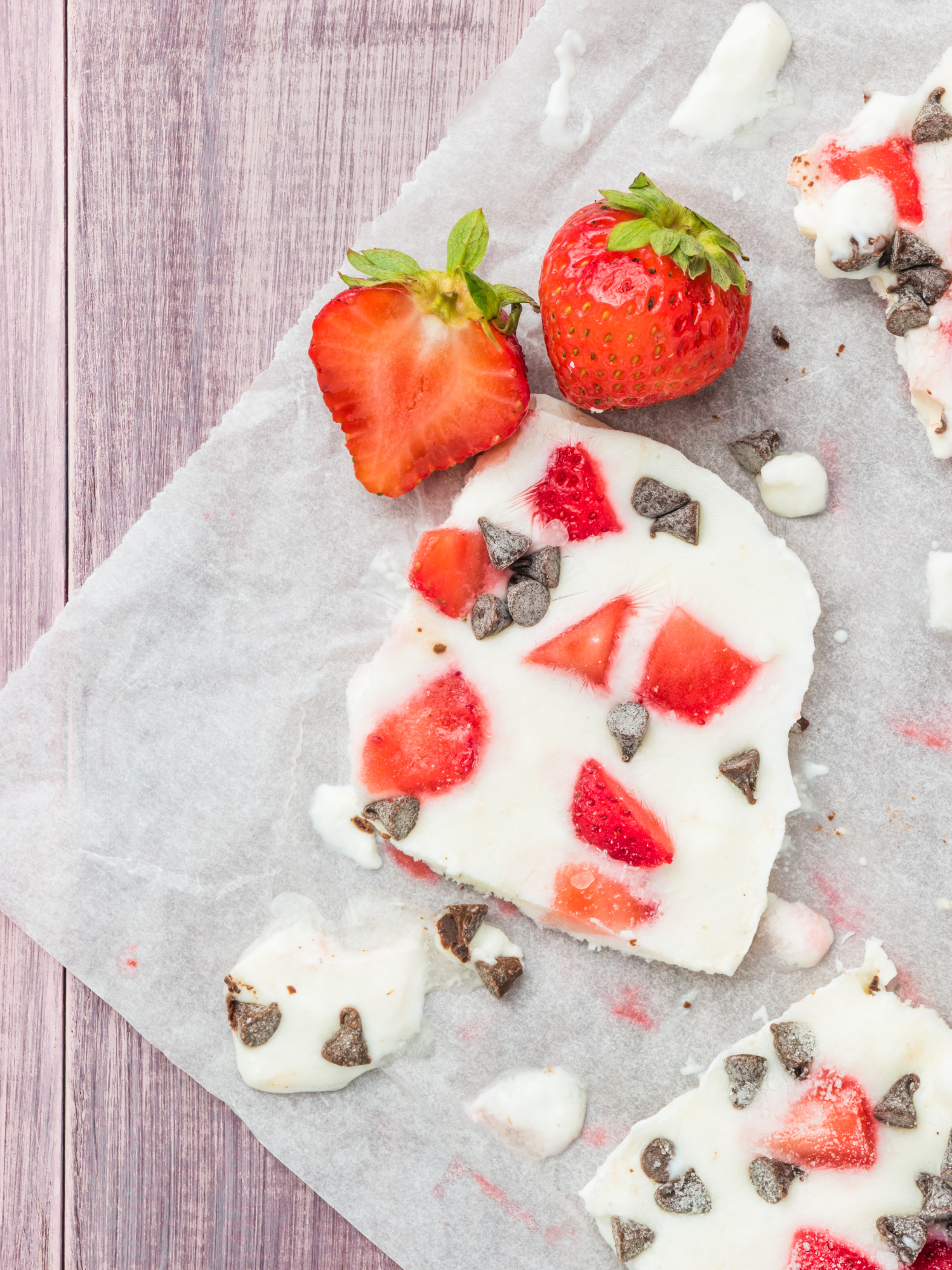 creamy yogurt bark with strawberries and chocolate chips sitting on a piece of parchment