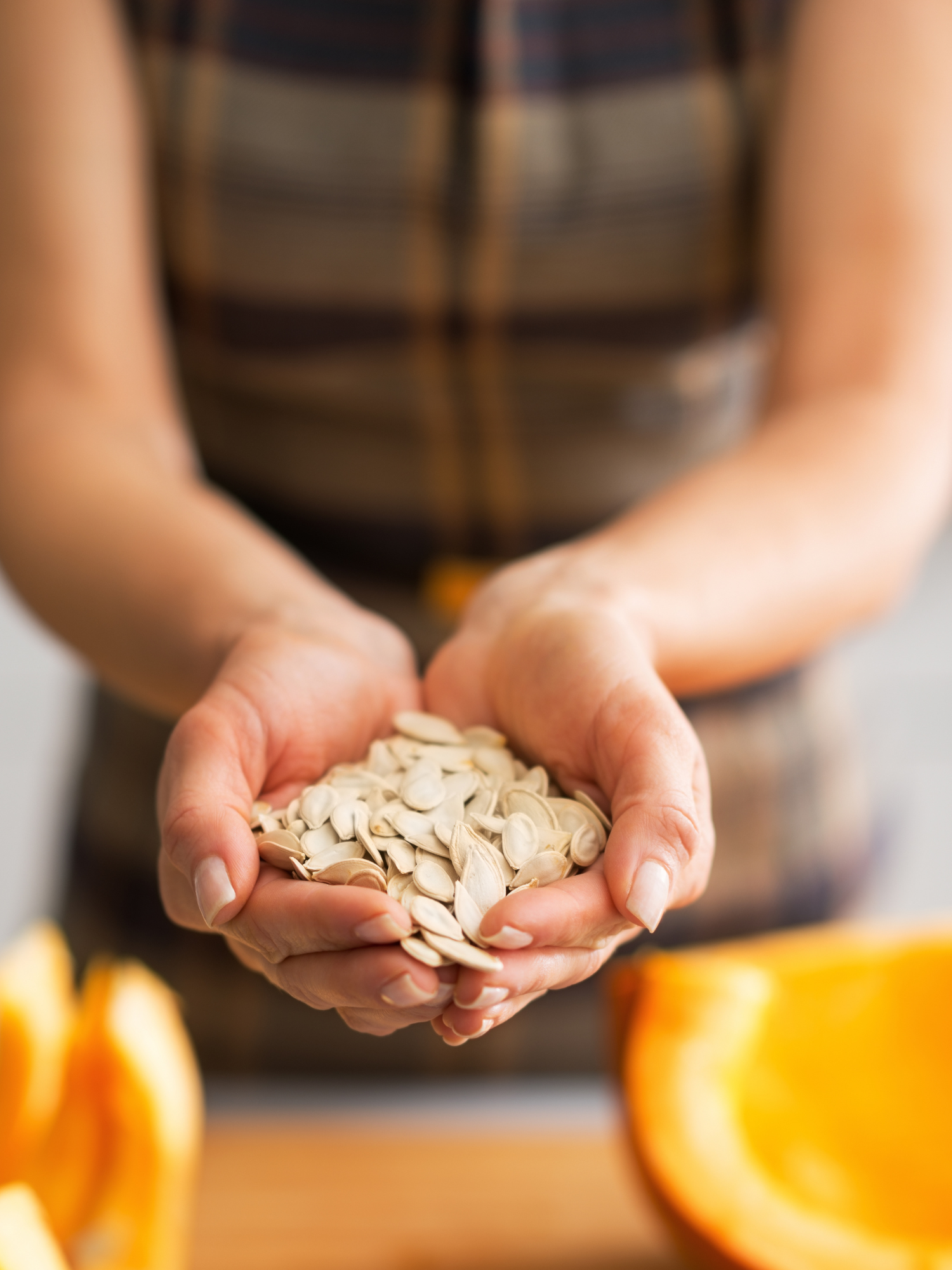 a woman extending a handful of butterntu squash seeds with an open butternut squash in front of her