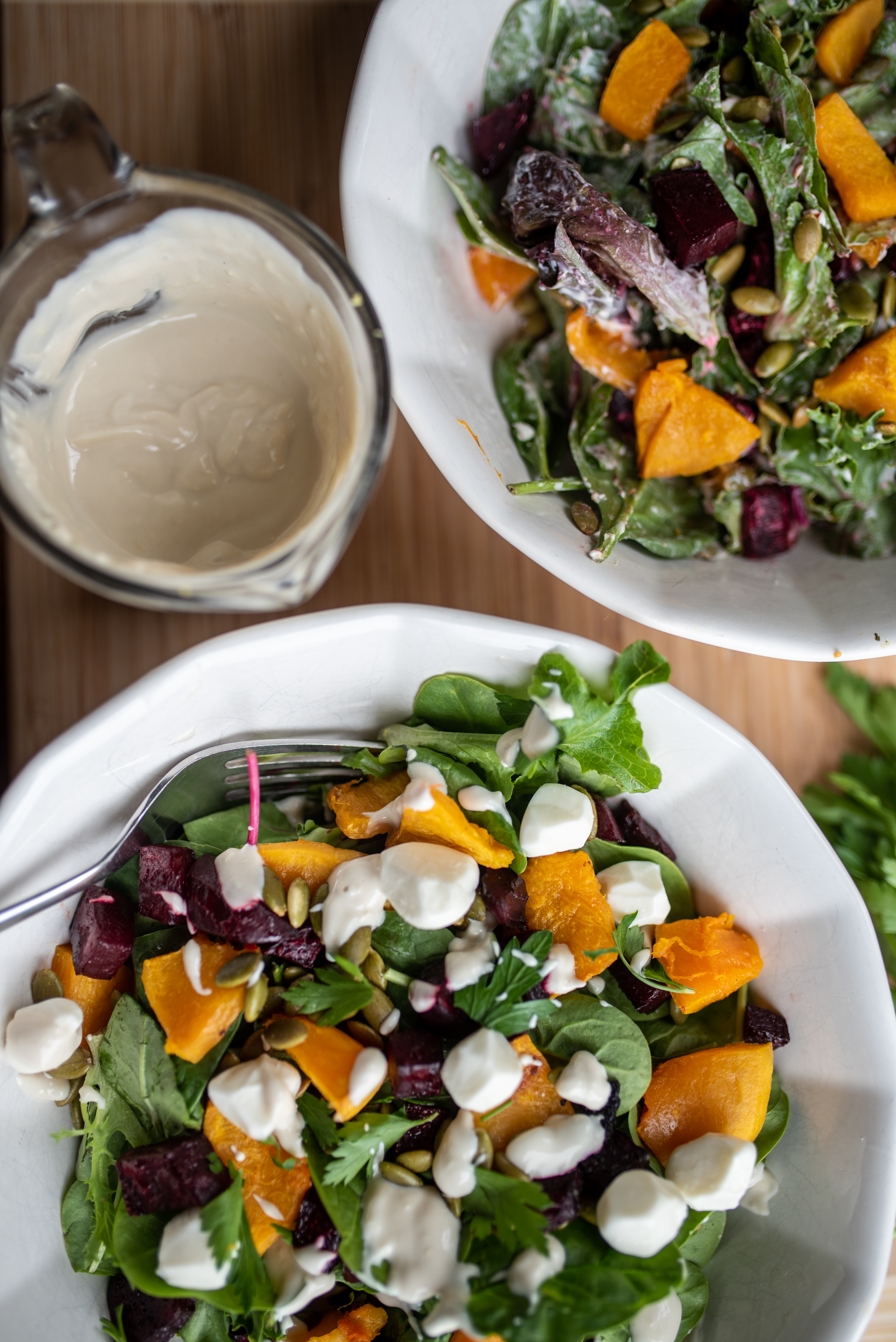 two bowls of beetroot and butternut salad with a small mixing glass of the low acid ginger and tahini dressing in between