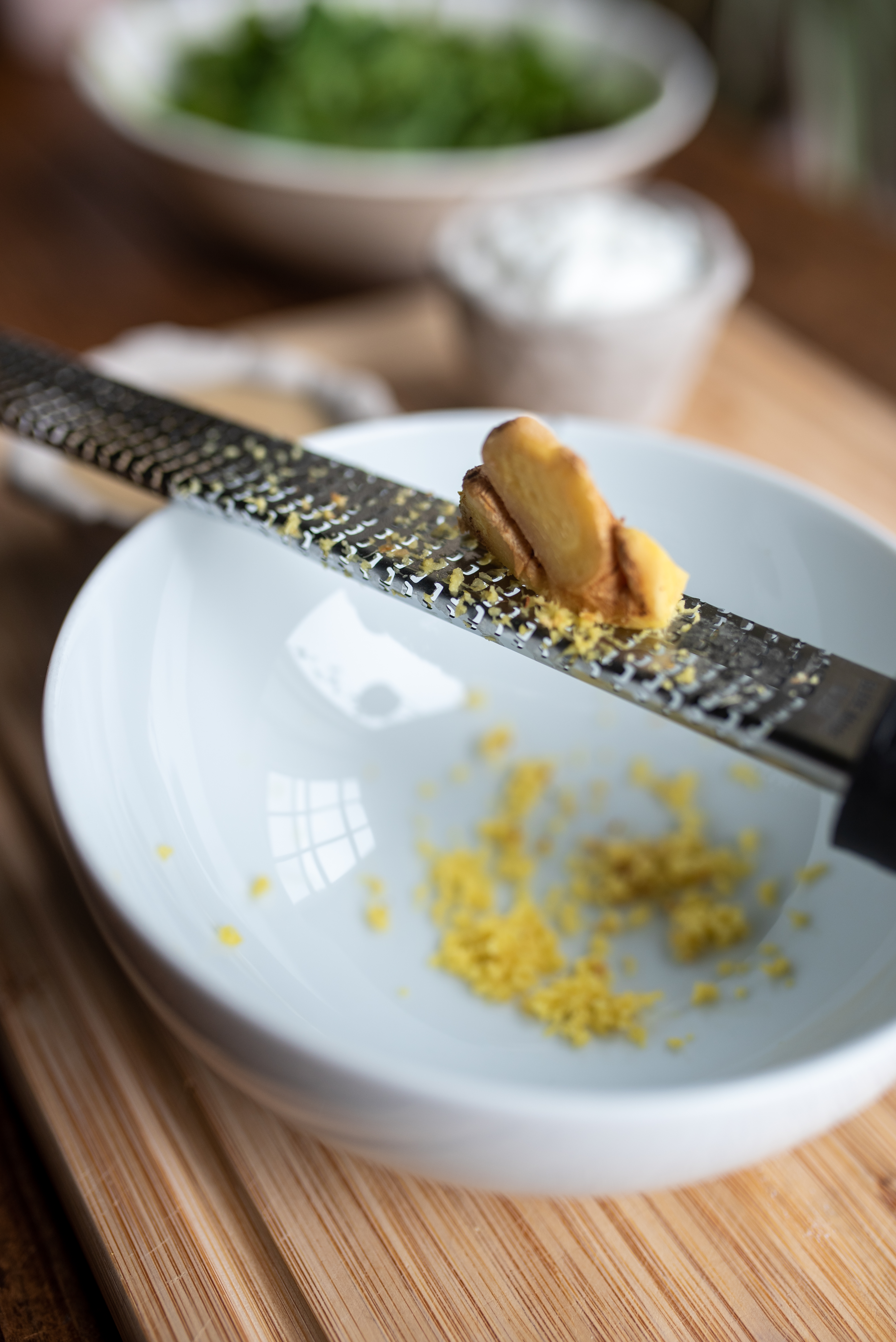 a piece of fresh ginger being zested into a white bowl