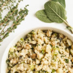 a white bowl of grain free thanksgiving stuffing surrounded by fresh sage and thyme