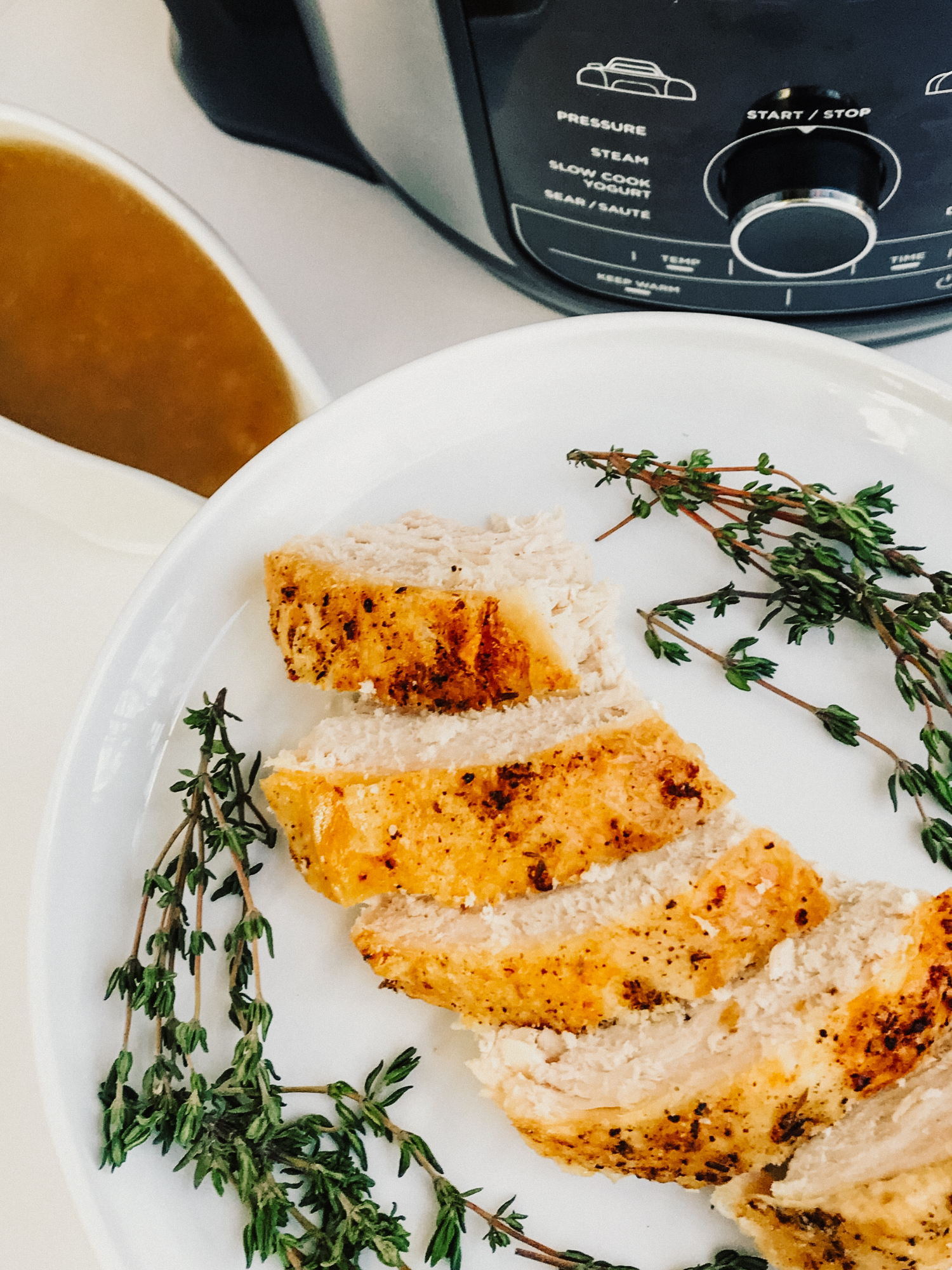 a a plate of sliced herbed turkey breast with a pressure cooker and gluten free gravy in the background